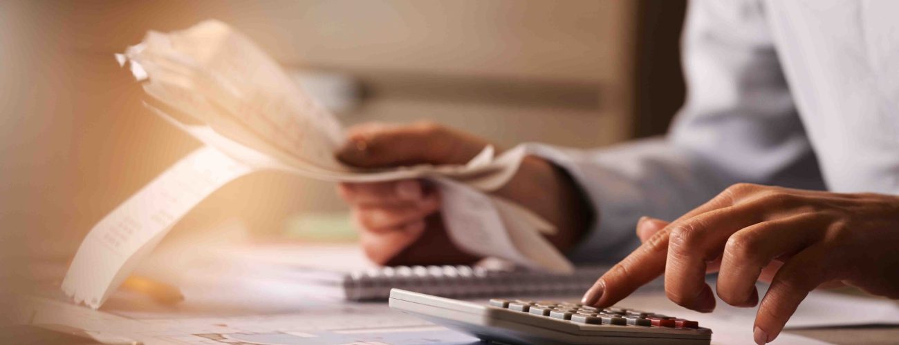 Close-up of economist using calculator while going through bills and taxes in the office.